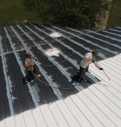 Two roof builders spray a new protective paint coating on a metal roof.