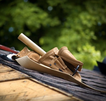 Several roofing tools including hammers, belts, nails, and clamps, sit on the peak of a roofing project.